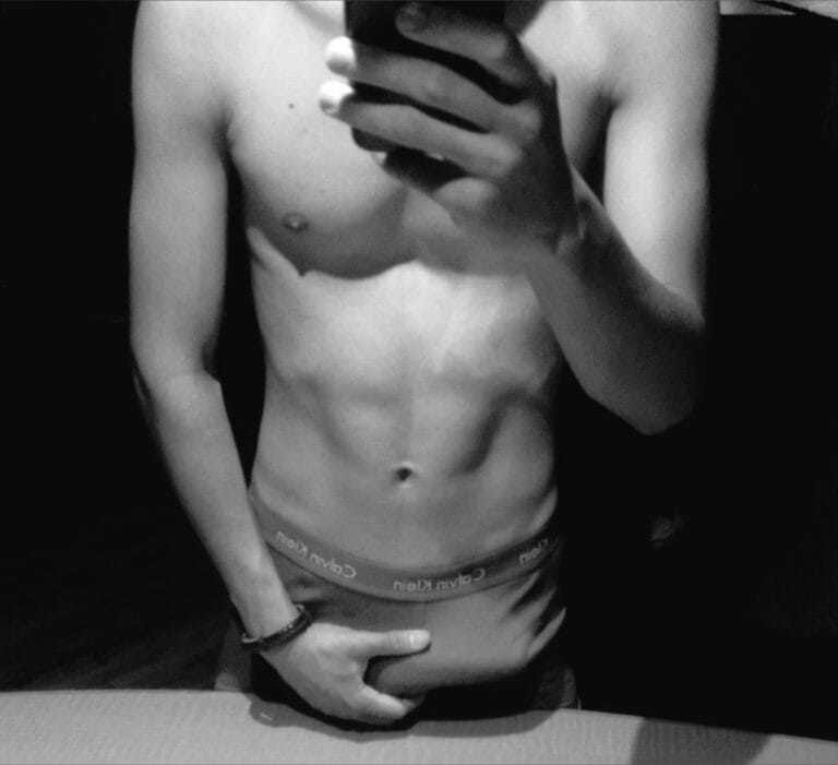 Black-and-white photo of a shirtless person sitting, hands clasped over the stomach; Calvin Klein waistband visible.